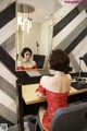 A woman in a red dress sitting at a desk in front of a mirror.